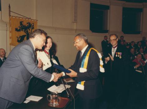 In 1982 krijgt de Senegalees Amadou-Mahtar M’Bow, hoofd van UNESCO, het 1ste Gentse eredoctoraat in de ontwikkelingssamenwerking, op voordracht van het ISVO. Op de achtergrond rechts promotor William De Coster (© Universiteitsarchief Gent, FA_04_018).